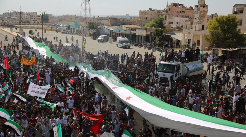 Сирийские демонстранты размахивают гигантским оппозиционным флагом во время массовой демонстрации против сирийского режима Башара аль-Асада в Саракибе