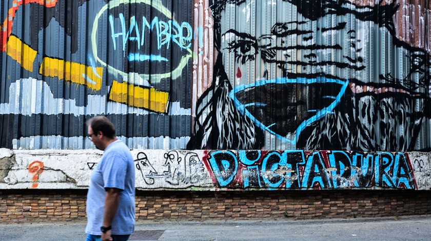 Граффити на стене в Каракасе, отражающее затянувшийся экономический кризис. Изображение девушки, закрывающей глаза и рот, слов «Голод» и «Диктатура» , Венесуэла, 30 ноября 2017 г.