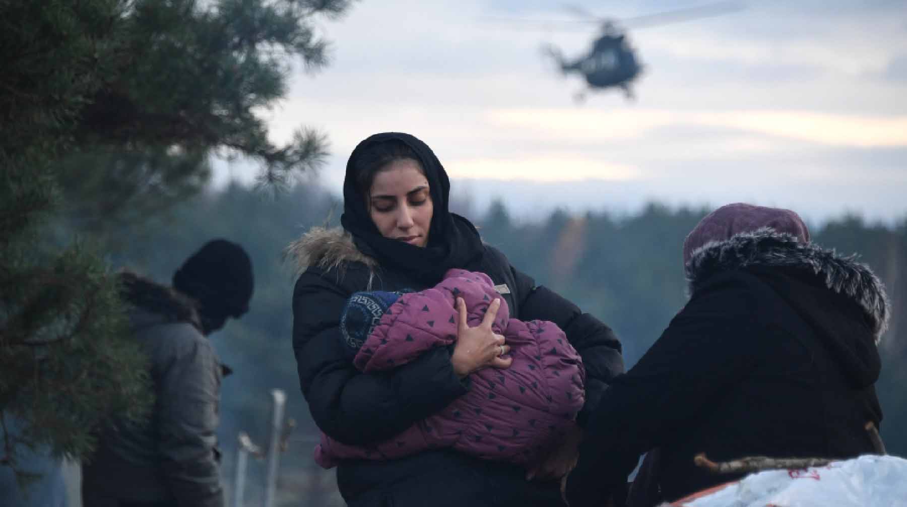 Женщина с ребенком в лагере у ограждения. Границу патрулируют на вертолете.