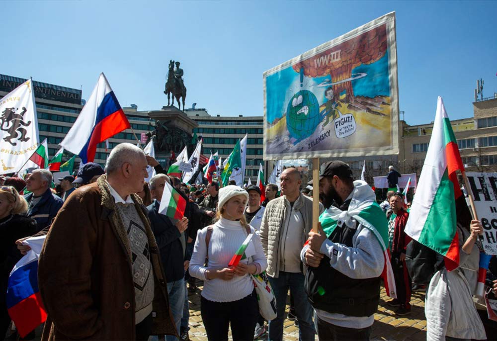 Участник митинга в Софии с плакатом, на котором изображена планета, Владимир Зеленский и ядерный гриб.
