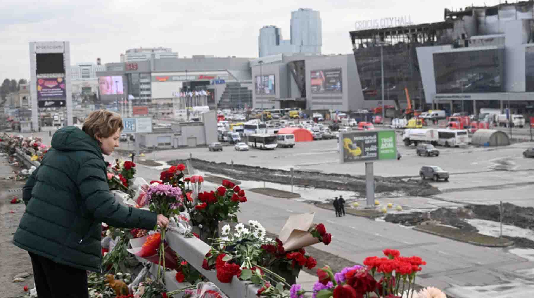 Женщина возлагает цветы у стихийного мемориала вдоль дороги у здания концертного зала "Крокус Сити Холл"